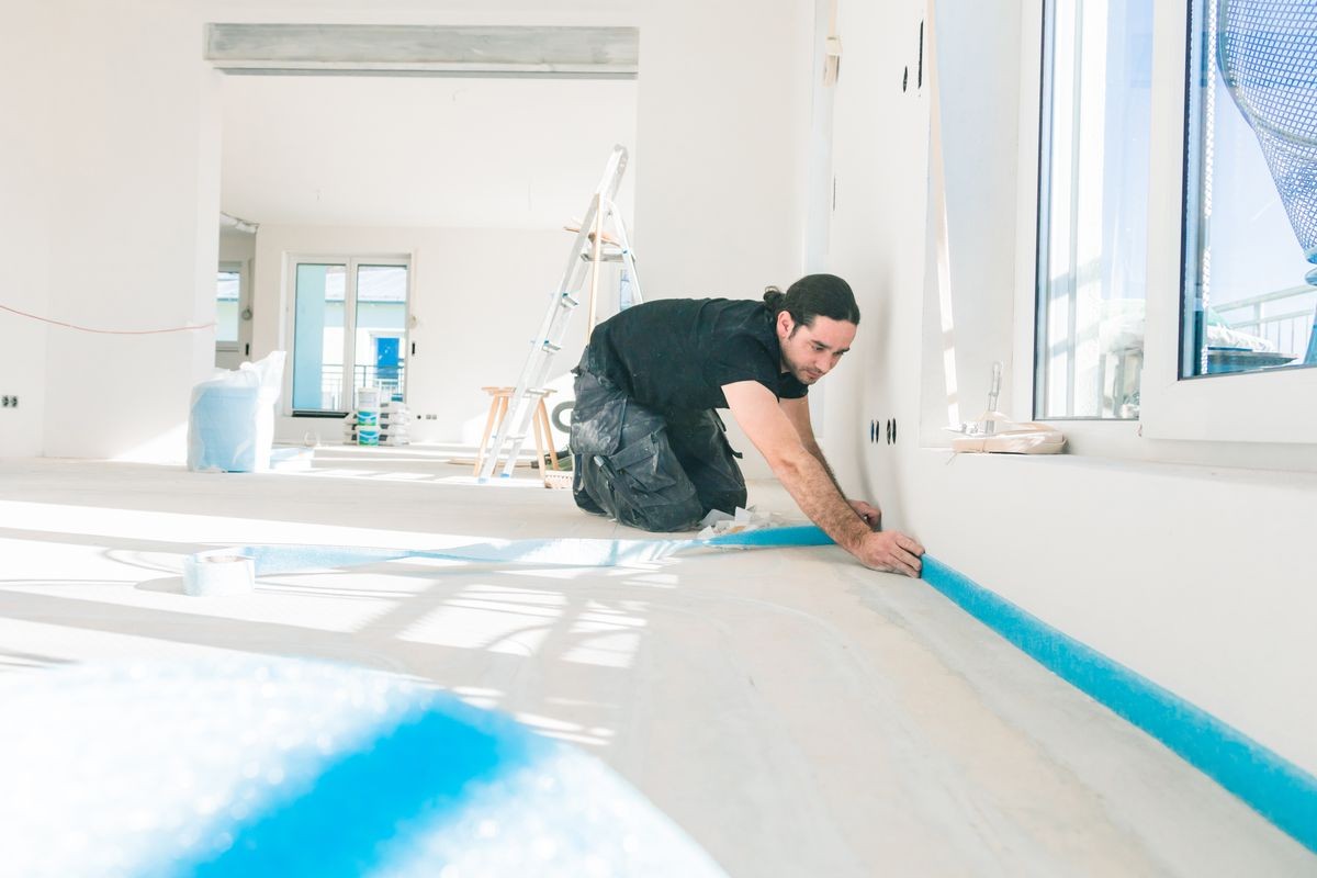 Workers in a flat work on a floor. glue edge insulation strip. balance the floor